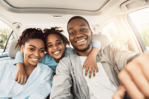Man in the driver's seat of a car, smiling with his family