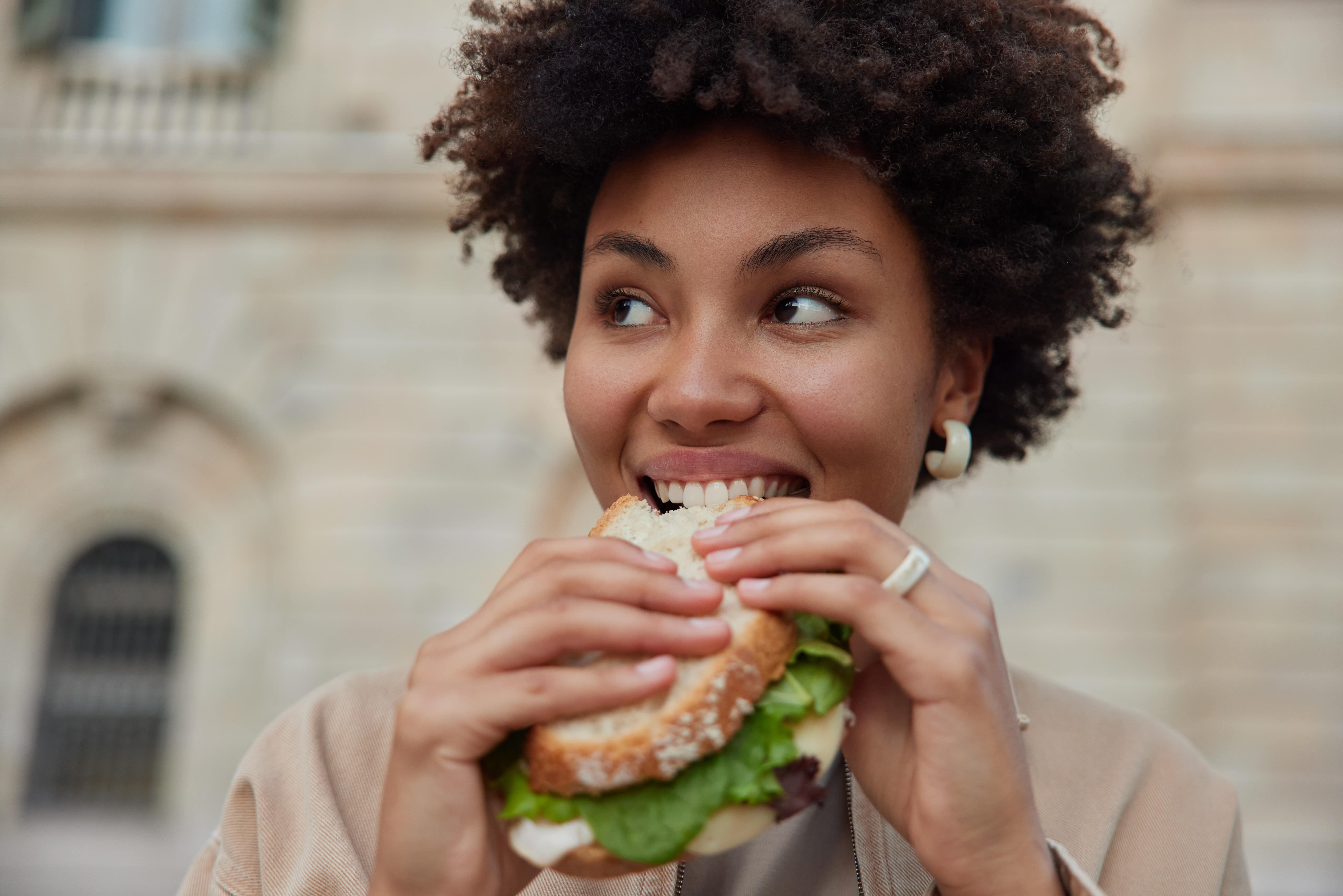 pretty curly haired woman bites delicious sandwich